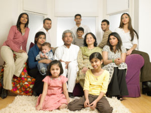 Large family gathered in a living room, spanning a variety of ages with different facial expressions (ranging from serious to smiling).