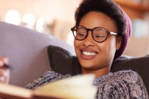 Shot of a young adult smiling and reading a book while relaxing on a sofa.