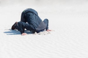 A person at the beach on their hands and knees with their head stuck in the sand.