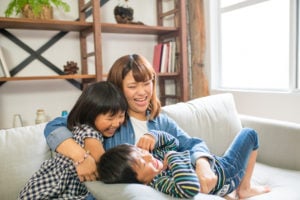 A smiling adult cuddling with two children on a sofa. 