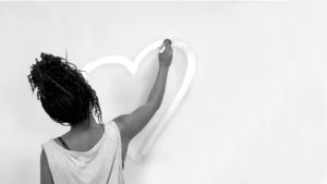 Shot of someone from behind painting a white heart on a grey wall.