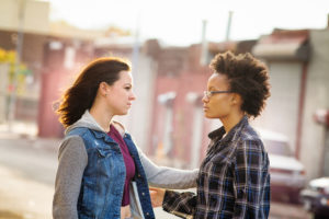 Young adult extends their hand to comfort a friend. They are standing in an urban setting.