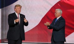 Trump and running mate Pence on a stage with the American flag on a display screen behind them.
