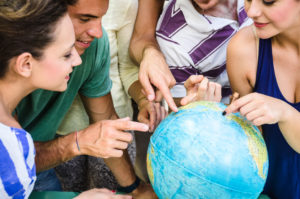 Students gathered around a globe, pointing to different places on the surface.