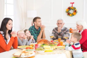 A family sits at a table, praying over Thanksgiving dinner together.