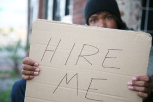"Hire me" sign held out by an unemployed person on a street.