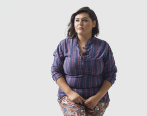 A fat person stands, looking uncomfortable and gazing uncertainly off to the side.