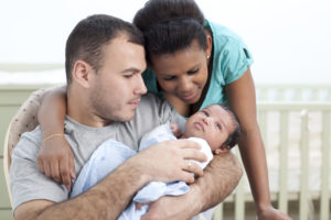 A biracial couple holds a newborn together.
