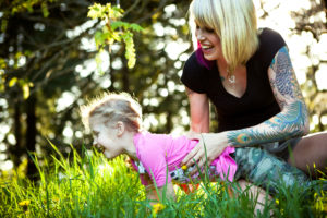 A parent with a full sleeve tattoo enjoys a day in the dark with their child, who crawls through the tall grass.