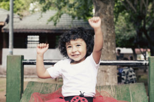A child with short, curly hair and a ladybug tutu plays on playground equipment.