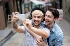 One person with their arms wrapped around the other, while they take a selfie together on a city street.