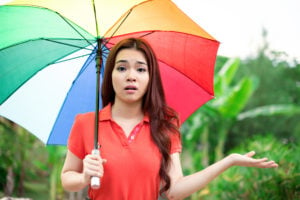 A person with a rainbow umbrella holds their hand out, looking quizzical.