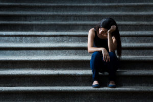 A person sits on stone steps and rests their head on their hand.