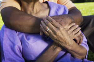A closeup on an older married person hugging their spouse from behind.