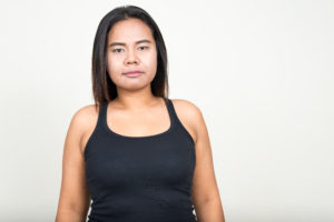 A person with a neutral expression and wearing a black tank stands in front of a white background.