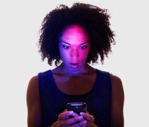 Person staring at a smart phone looking surprised. Color from the phone reflected on their face.