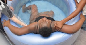 A pregnant person lies in a birthing pool, supported by two midwives.