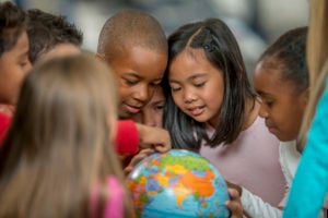 A group of schoolchildren gather around a globe.