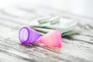 Two menstrual cups at the forefront with pads and tampons positioned in the background