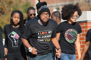 Jonathan Butler and Mizzou students holding hands in front of an obstructed brick structure.