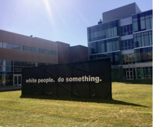 An art piece by Kara Springer of Temple University’s School of Art reads in white text on a black background, “white people. do something.”