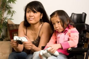 A parent and child playing video games together. The child is in a wheelchair.