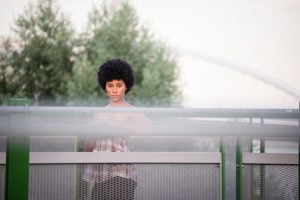 Person with an afro standing on a bridge with a serious facial expression