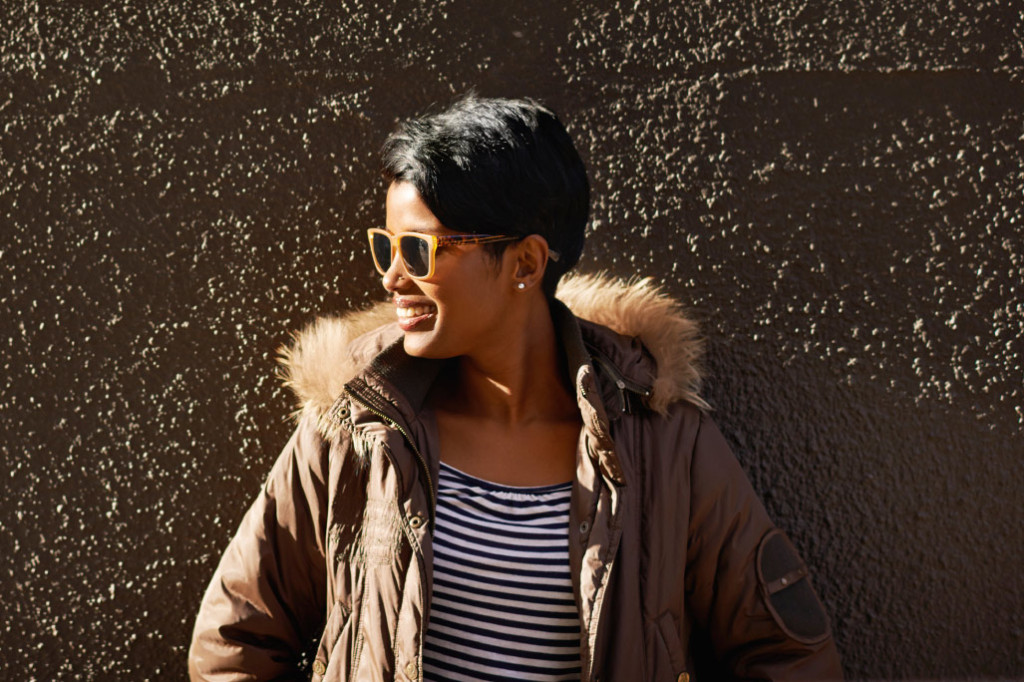 A person with short hair and sunglasses looks to their side while smiling.