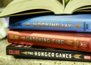 The three books in the Hunger Games series laid out on a table in a pile with another book open on top
