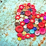 A collection of colorful buttons make a heart shape over a distressed teal table top