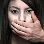 One person staring ominously straight while another's hand is placed over their mouth, quieting them