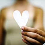 Person holding up a piece of paper that's been cut into a heart shape