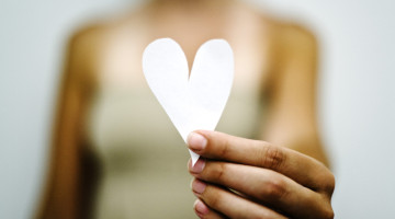 Person holding up a piece of paper that's been cut into a heart shape