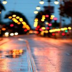 A wet, rainy street at night with colorful street lights blurred in the distance