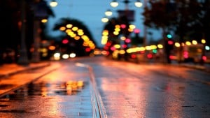 A wet, rainy street at night with colorful street lights blurred in the distance