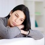 Person sitting on a couch, leaning against their own arms, looking worried or contemplative