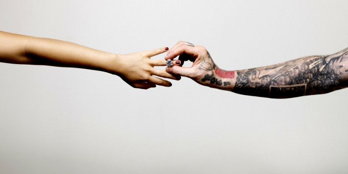 One tattooed arm outstretched to place an engagement ring on the finger attached to another outstretched arm