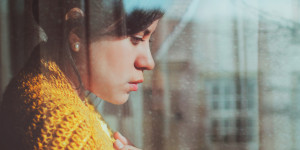 Person standing at a window, looking out and down, seemingly sad or contemplative