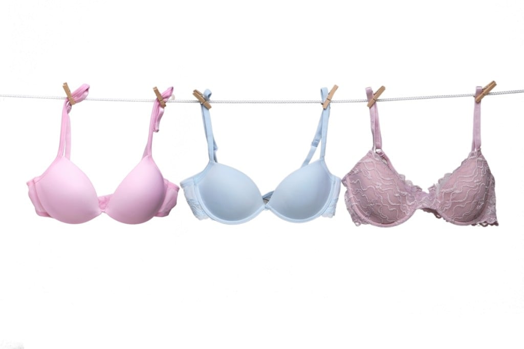 Three bras – one pink, one powder blue, one taupe – hang on a line by clothes pins