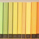 Books lined up on a shelf in order by color, creating a rainbow