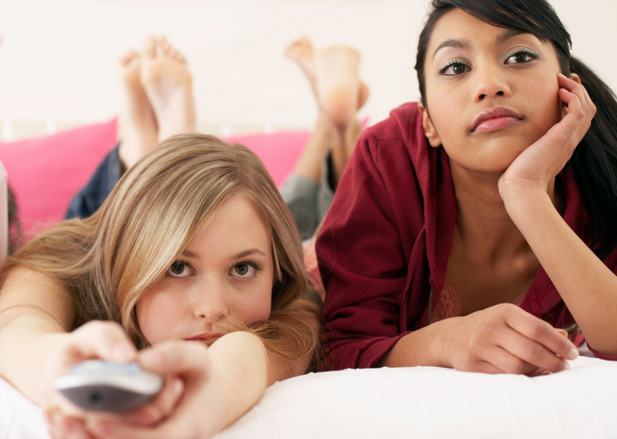 Two teenagers watching TV, looking dissatisfied