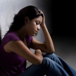 Young person sitting against a wall with their head in their hands, visibly upset