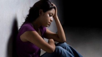 Young person sitting against a wall with their head in their hands, visibly upset