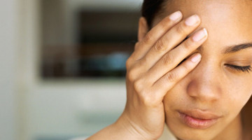 Feminine-presenting person with their hand over their face looking tired.