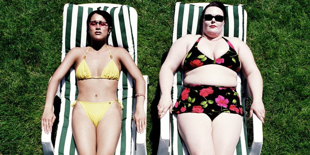 An elevated view of a thin person and a fat person lying side by side on lounge chairs