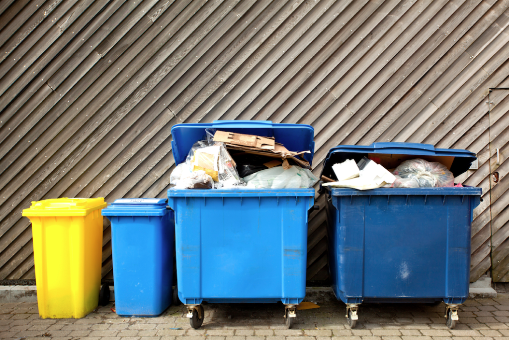 A bunch of dumpsters and recycling bins behind a building