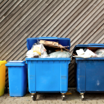 A bunch of dumpsters and recycling bins behind a building