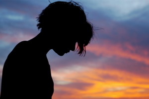 Silhouette of a person looking down, against a sunset