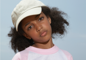 Young child in a baseball cap, looking frustrated at the camera