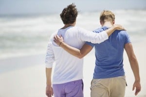 A rear view of two people walking down the beach with their arms around one another